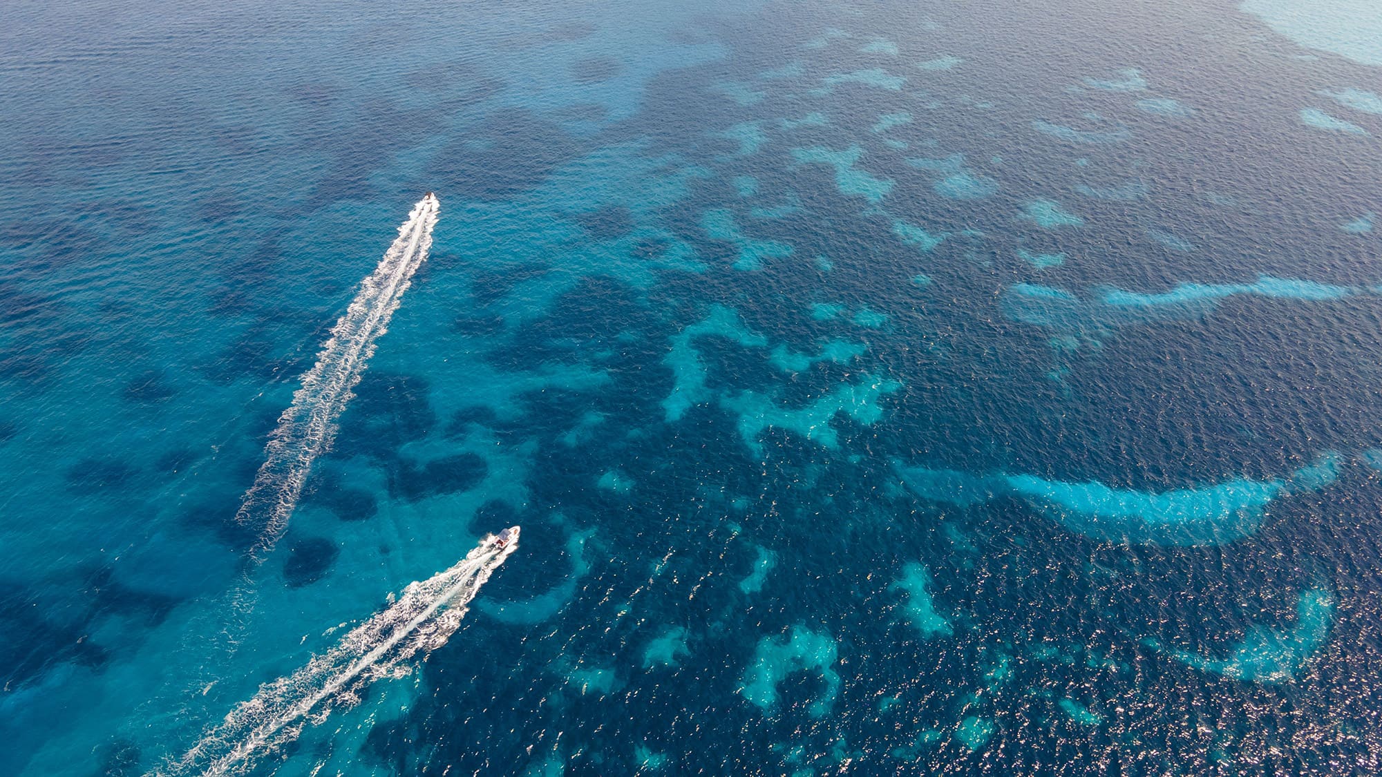 An aerial of two motor boats drawing water trails